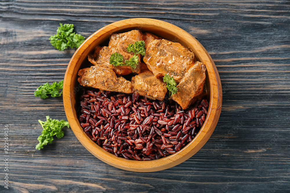 Bowl with tasty boiled rice and meat on wooden table