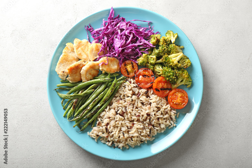 Plate with boiled rice, vegetables and meat on grey background