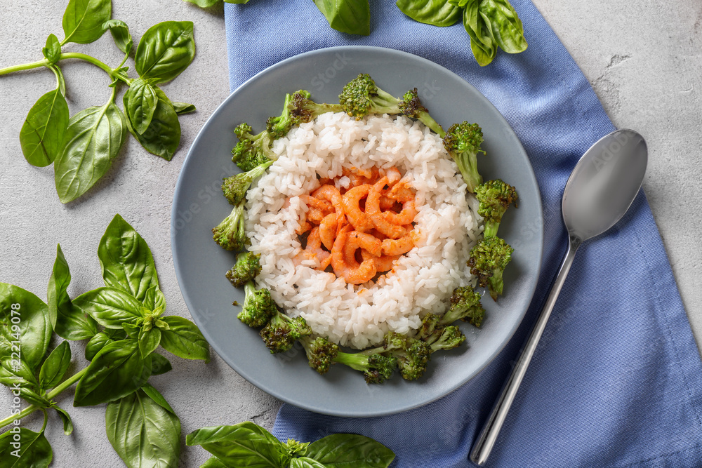 Plate with boiled rice, broccoli and shrimps on grey background