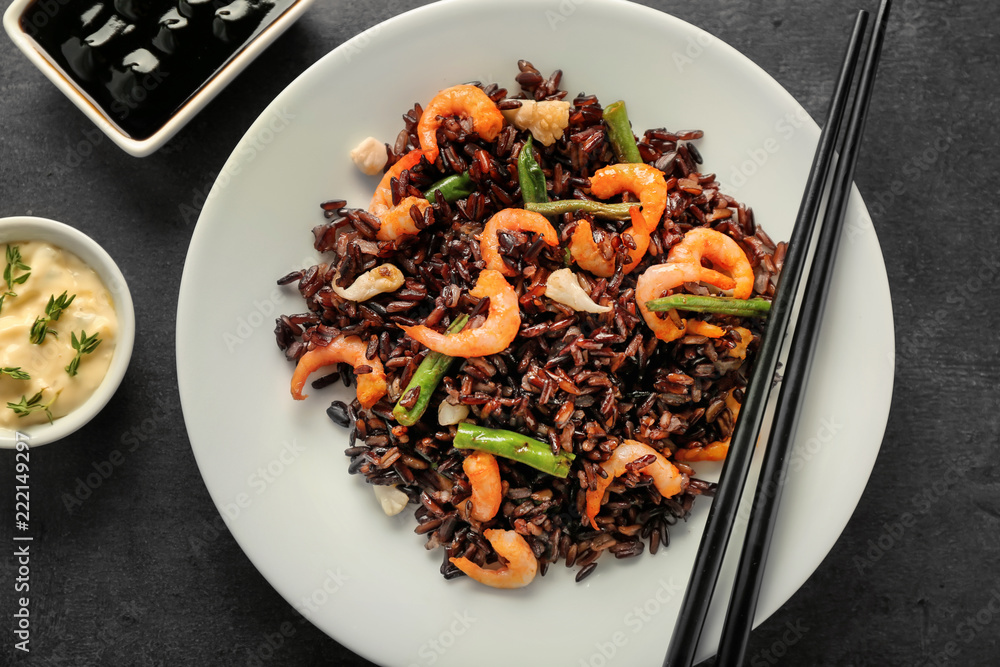 Plate with boiled rice, shrimps and vegetables on dark table