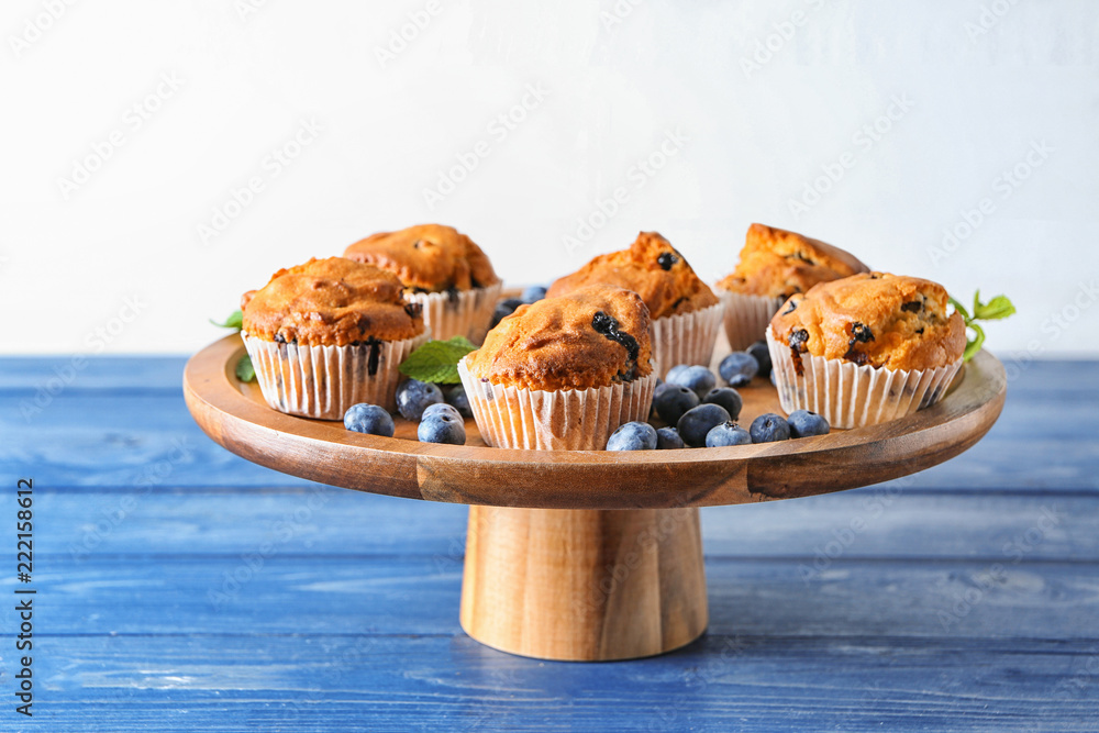 Stand with tasty blueberry muffins on color table