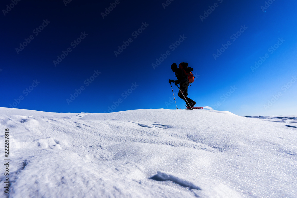 背着背包的男人穿着雪鞋在冬季风景中行走的剪影。在雪地里徒步旅行，大雪纷飞