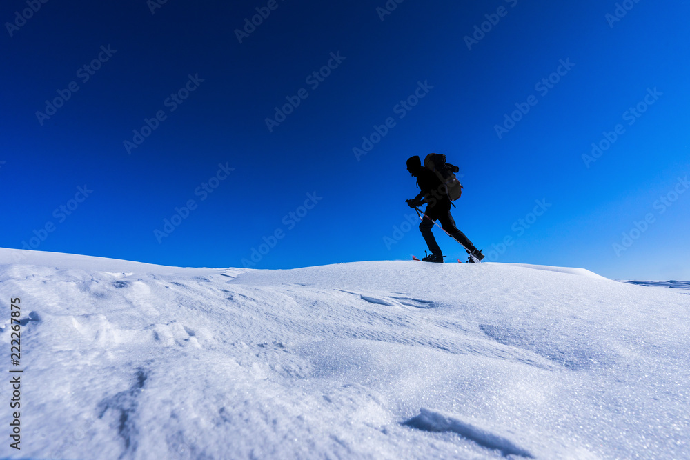 背着背包的男人穿着雪鞋在冬季风景中行走的剪影。在雪地里徒步旅行，雪地