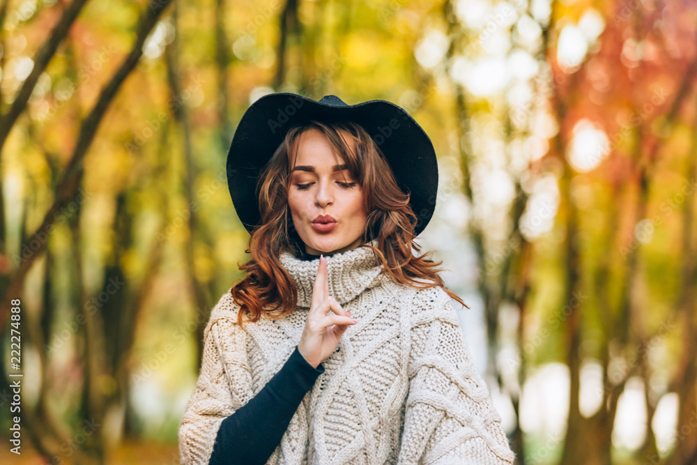 beautiful girl in a hat with curly hair holds her hand in front of her in the park in the autumn