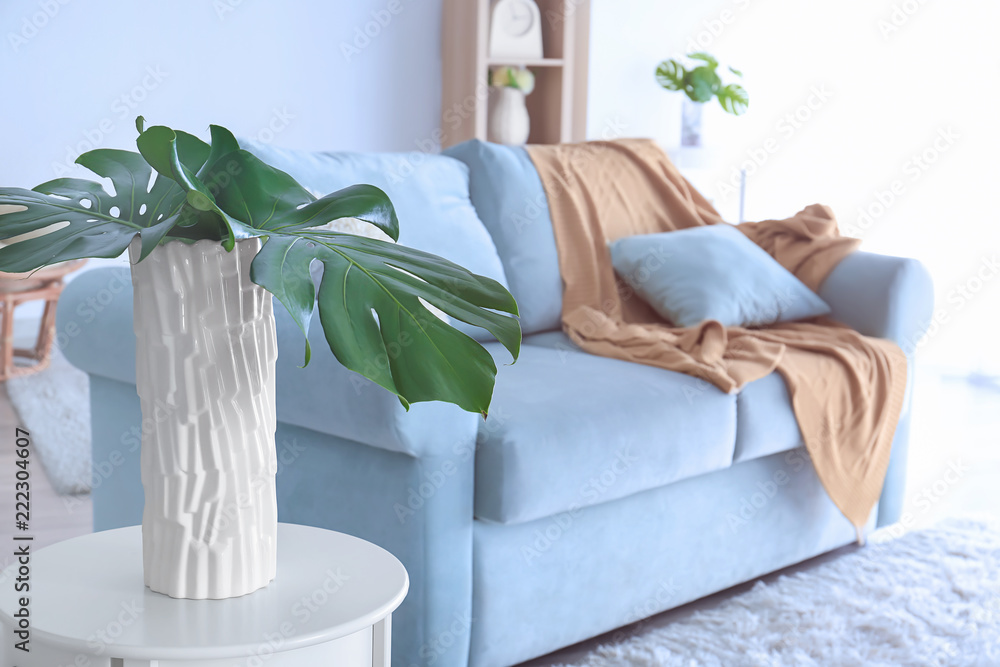 Vase with tropical leaves on table in interior of stylish room