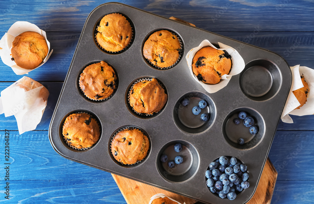 Baking tin with muffins and blueberry on color table