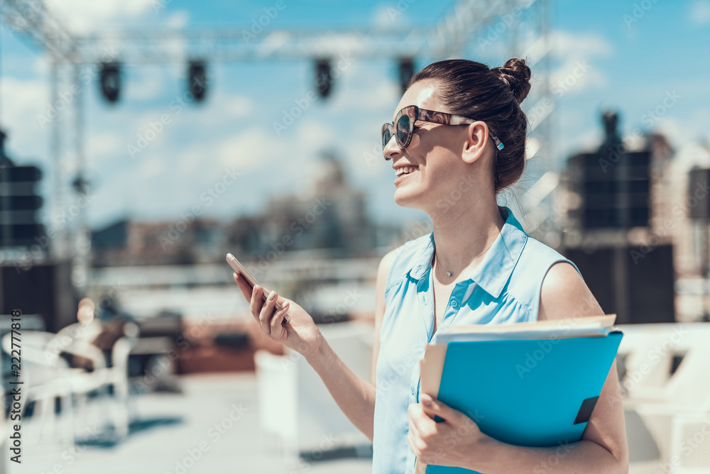 Side view beaming businesswoman holding contemporary phone and folders with information in hands. Sh