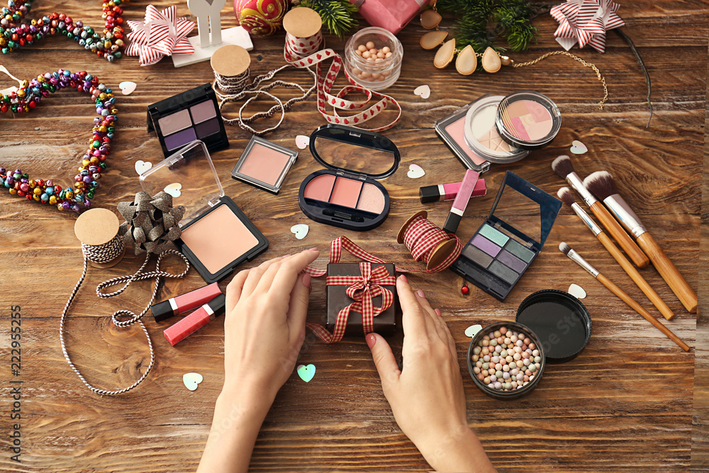 Woman with Christmas present and set of decorative cosmetics on wooden background