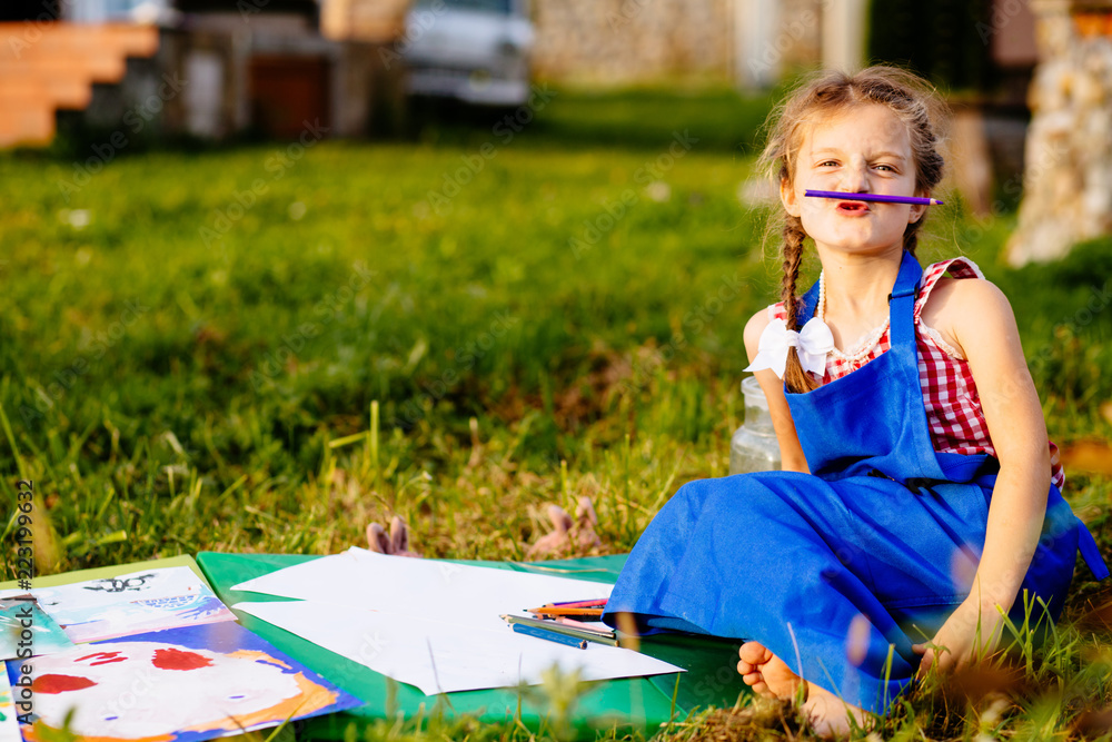 Portrait of cute playful child girl sitting on the grass in a summer garden painting with pensil, Ed