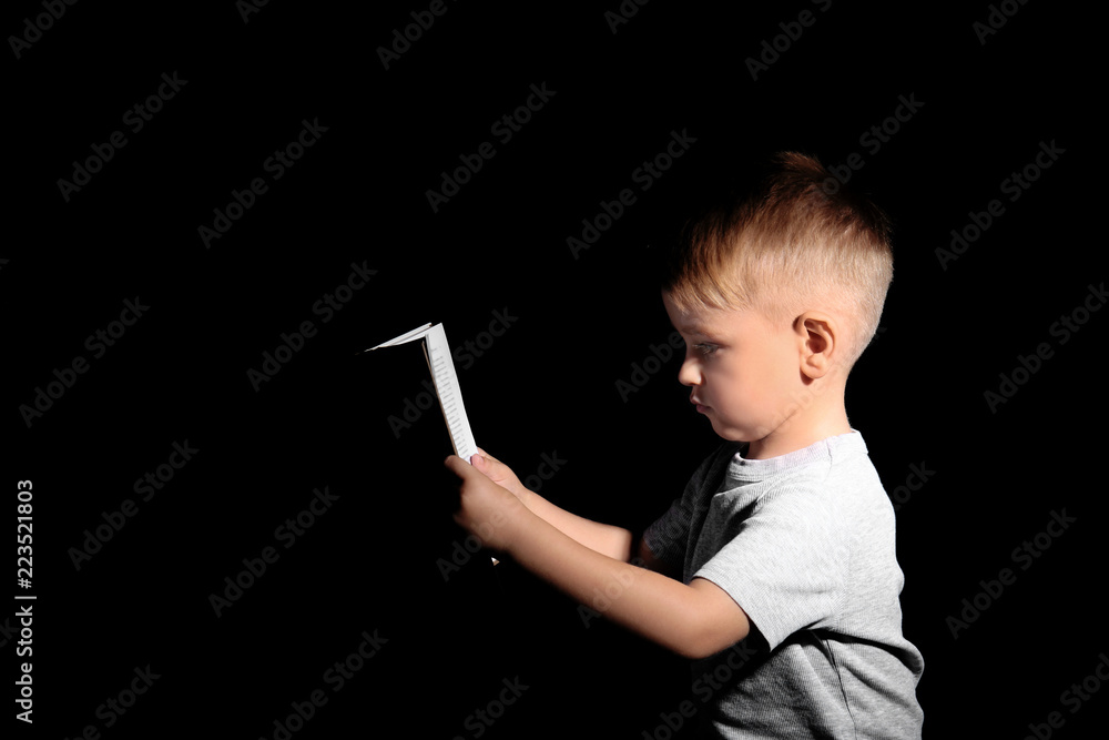 Cute little boy reading book on dark background