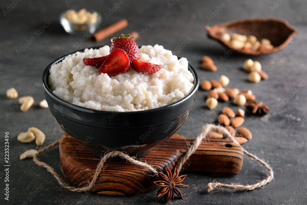 Bowl with delicious rice pudding and strawberry on dark table