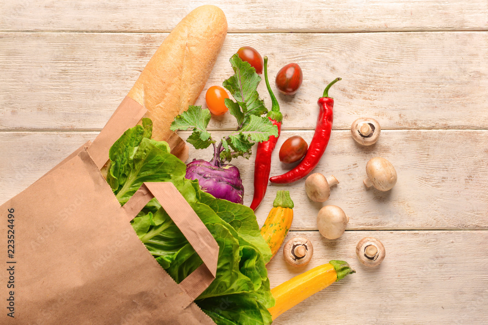 Paper bag with various fresh vegetables and baguette on wooden background