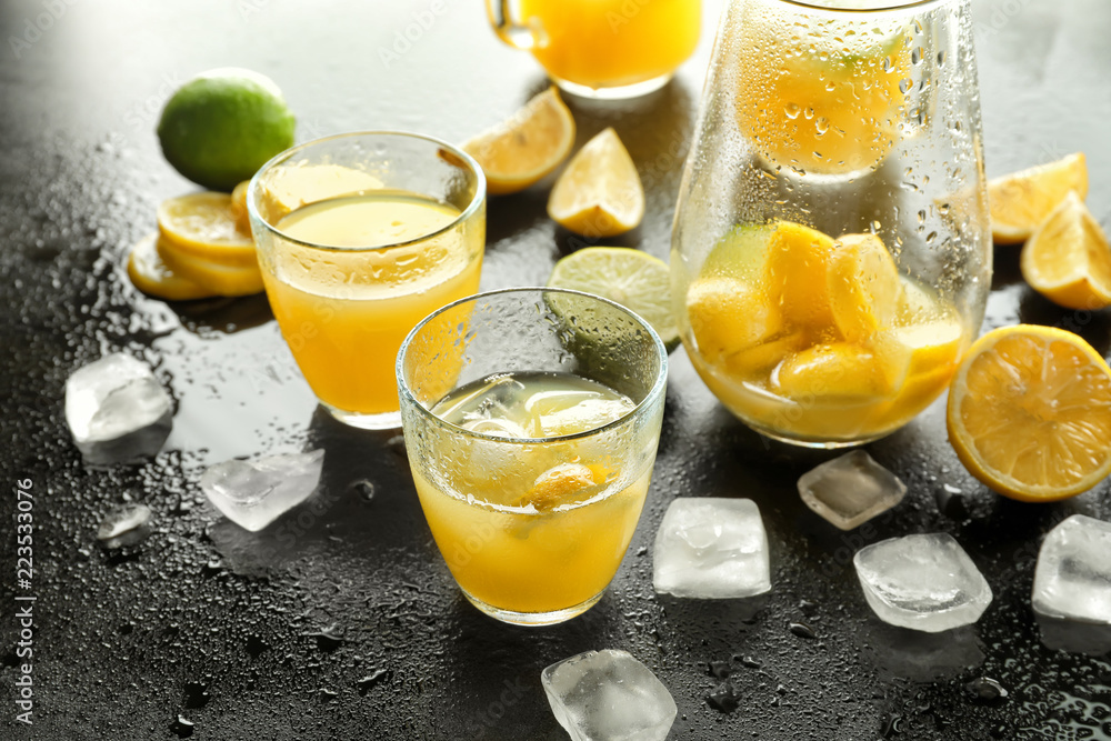 Glasses of fresh lemon juice with ice cubes on dark table