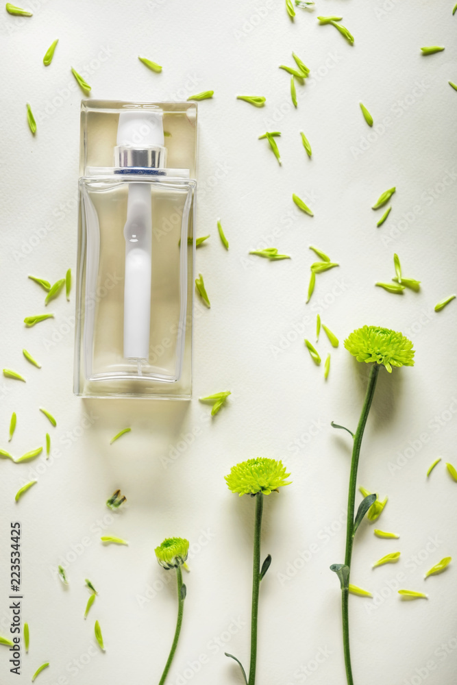 Transparent bottle of perfume with beautiful flowers on light background