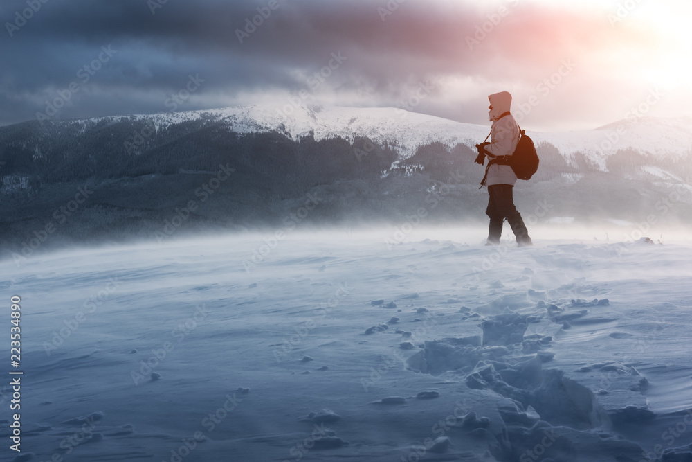 冬天独自一名摄影师背着背包在暴风雪中登上山顶。旅行概念。鲤鱼