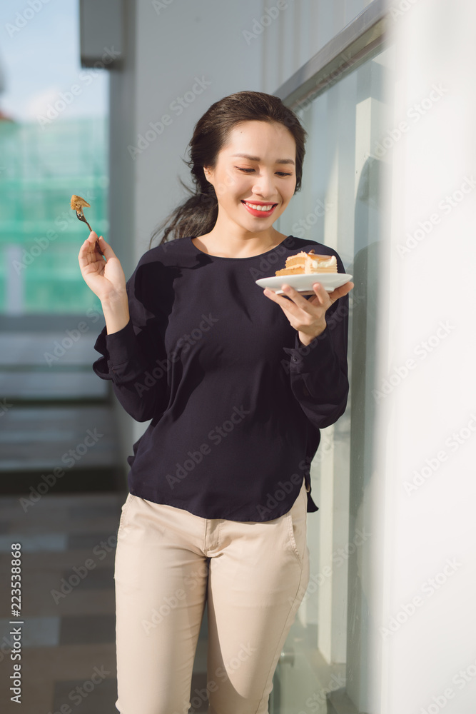 Young happy woman stands on the terrace of the hotel with dish cake in the morning. Pretty asian gir