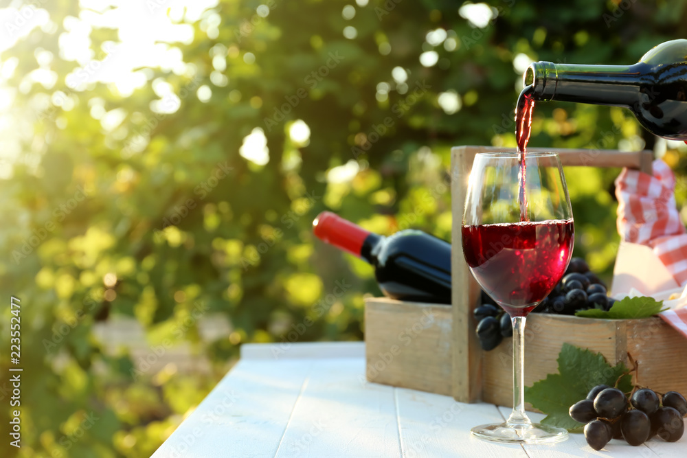 Pouring of red wine into glass on table in vineyard