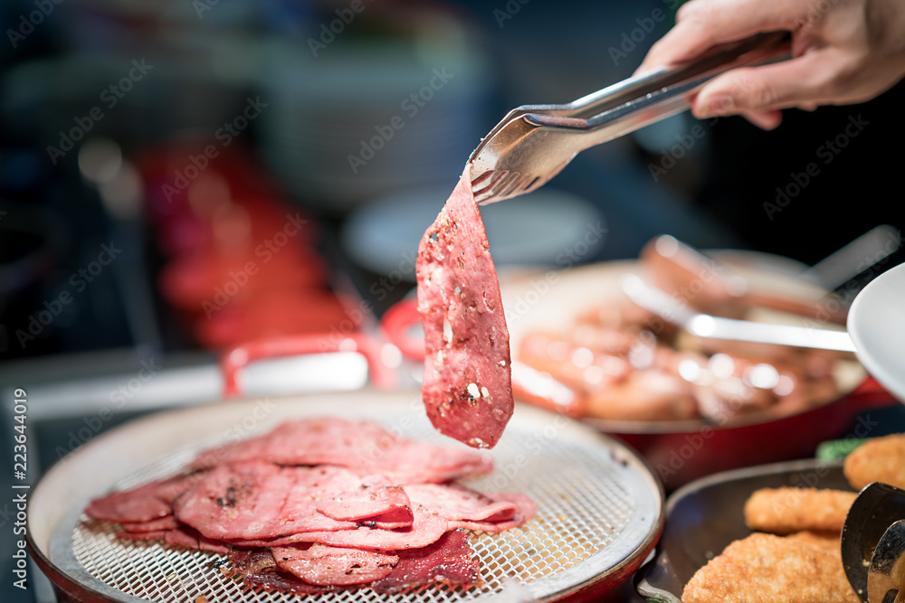 酒店餐厅的酒吧里，人们用手拿着钳子夹在一盘烟熏肉片上。早餐a