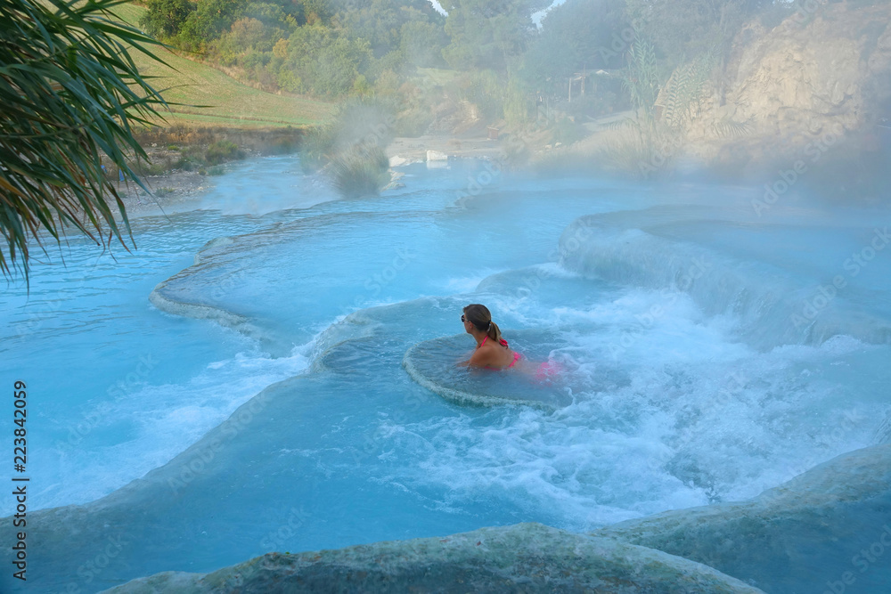 Young woman rests on a white stone ledge in invigorating thermal baths in Italy.