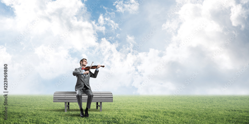 Handsome businessman in park on wooden bench play his melody