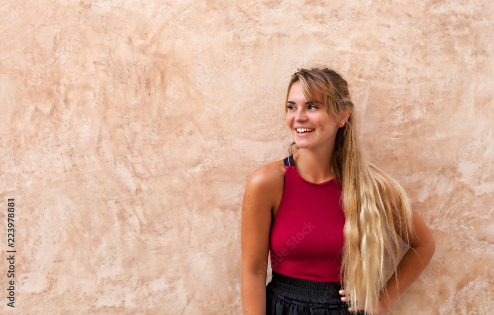 Cheerful beautiful young woman posing against wall on the street