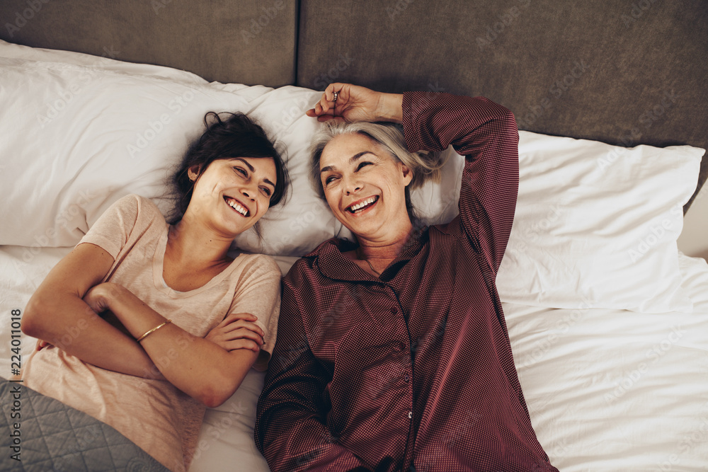 Happy mother and daughter lying on bed together and talking