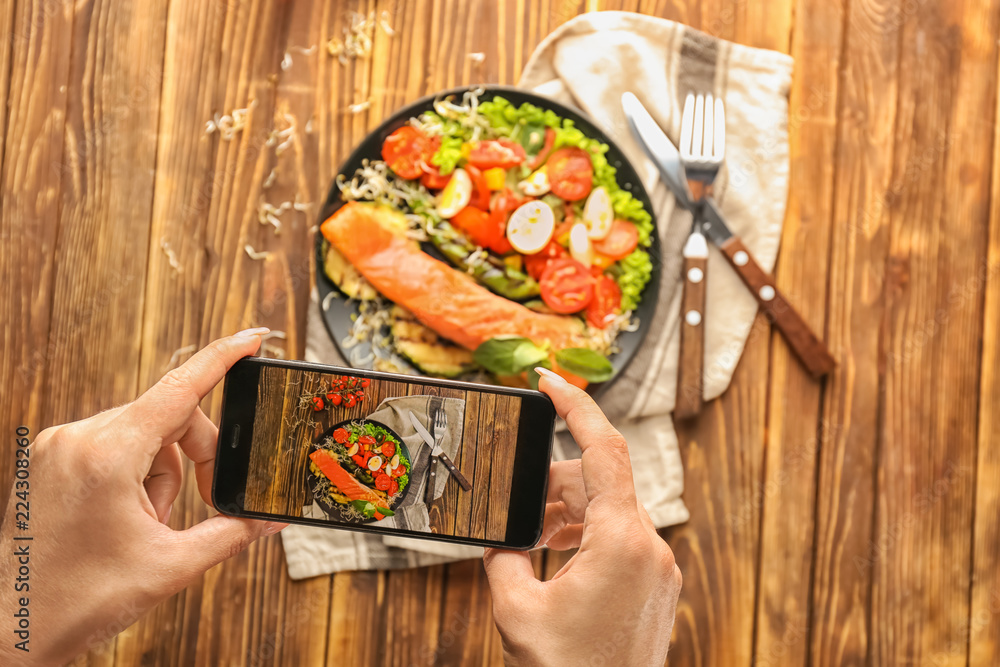 Woman taking photo of tasty salmon with fresh salad, closeup