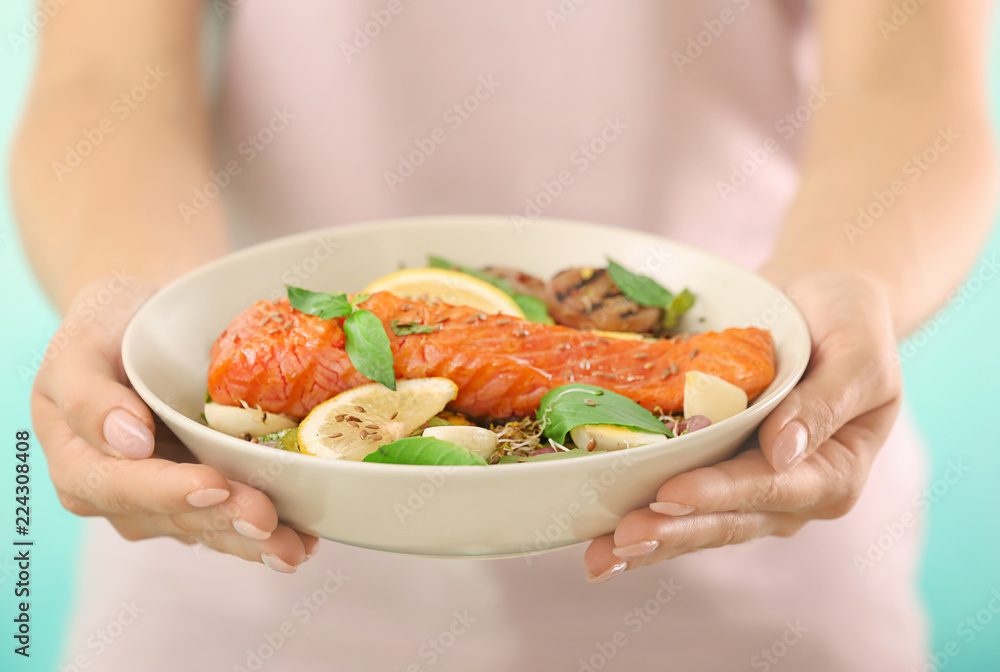 Woman holding plate with tasty salmon and fresh salad, closeup