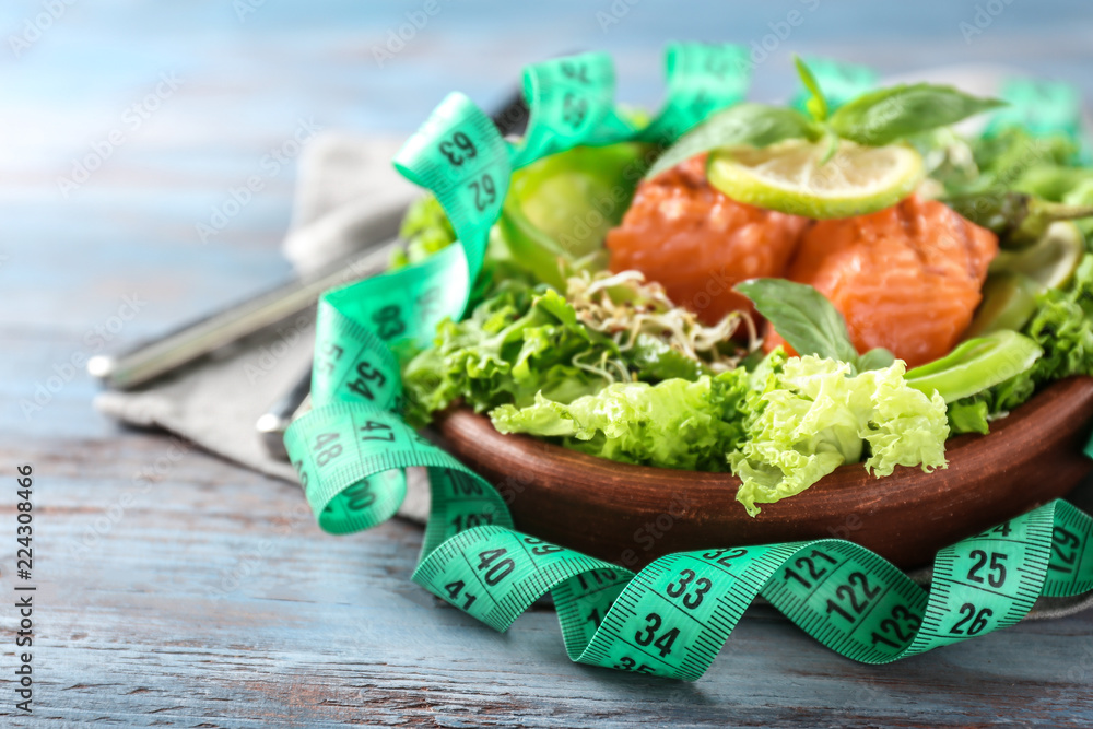 Plate with tasty fresh salad and measuring tape on wooden table. Diet concept