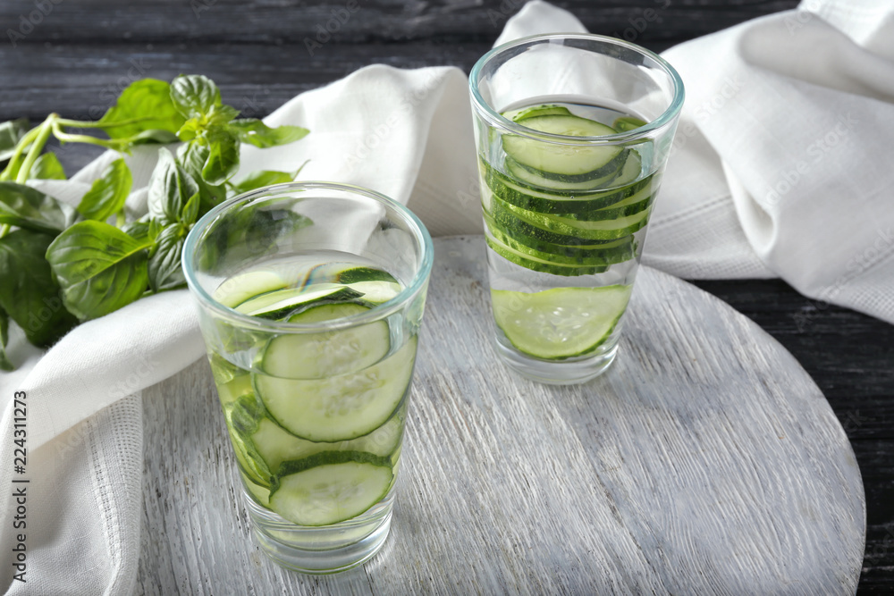 Glasses of fresh cucumber water on wooden board