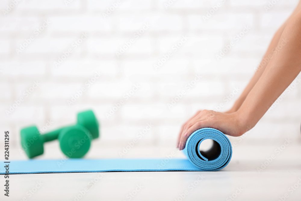 Young woman rolling yoga mat indoors