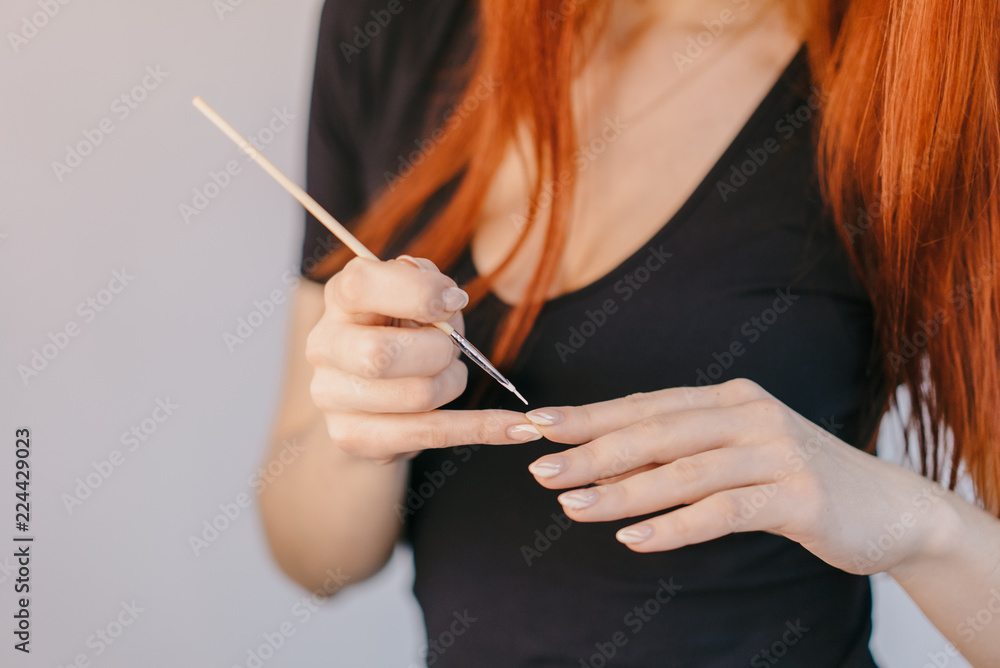 woman varnishes nail using a thin brush on her fingers. Close-up