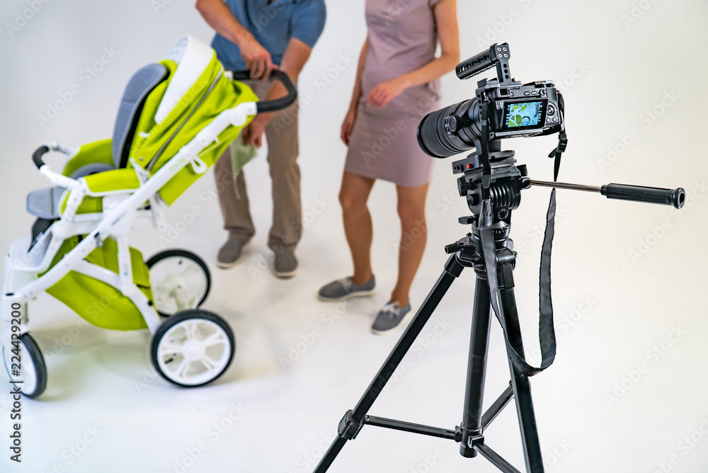 camera stands on a tripod on the background of man and woman near green stroller in the studio