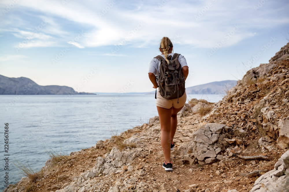 Hiker girl with backpack hiking on trail along sea bay