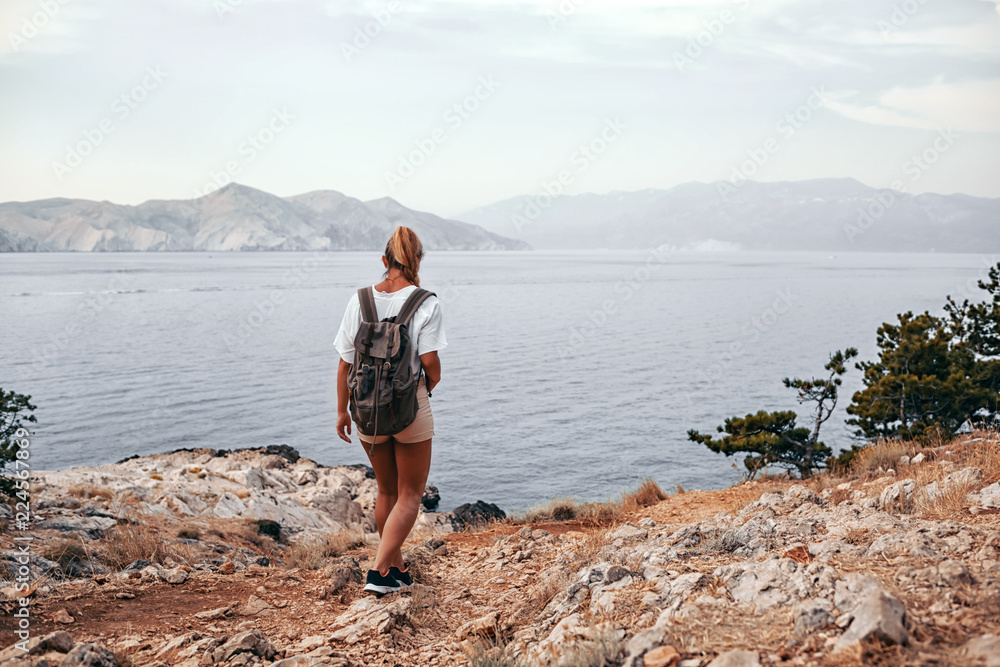 背着背包的徒步女孩沿着海湾徒步旅行