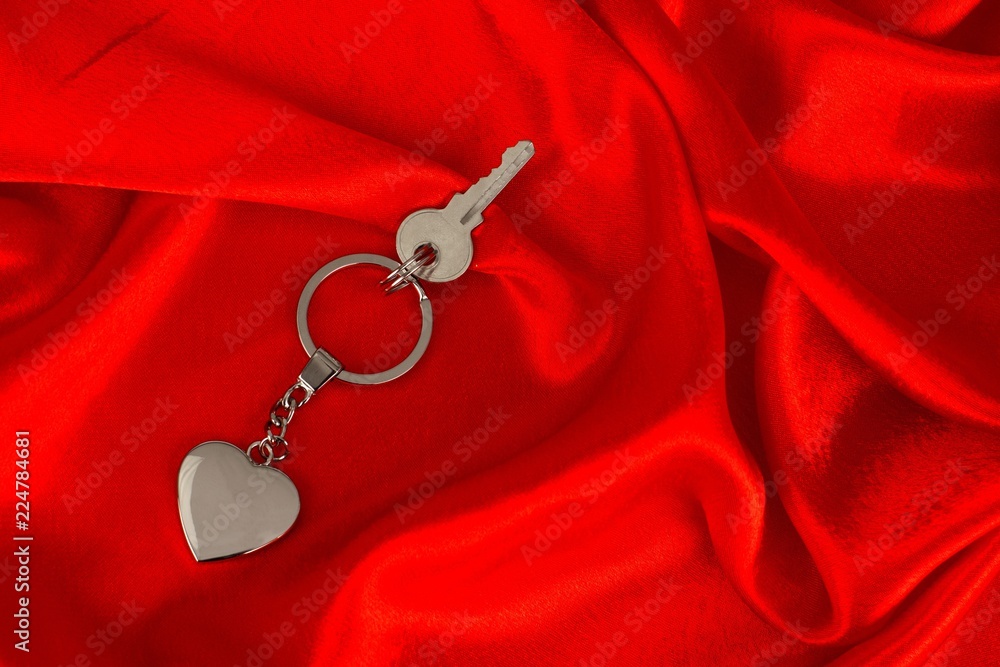 Heart shaped keychain and a key on red, satin background