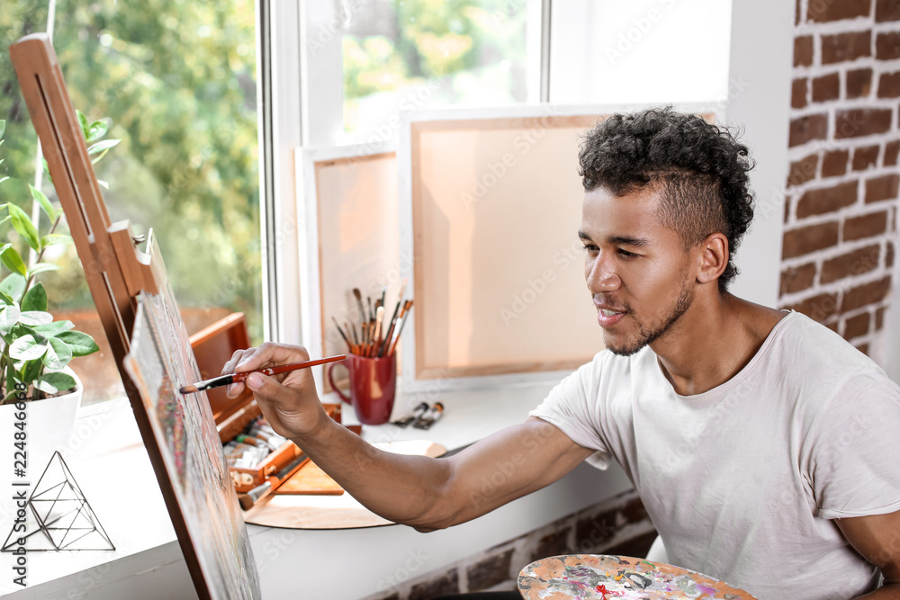 Young African-American artist painting picture in workshop