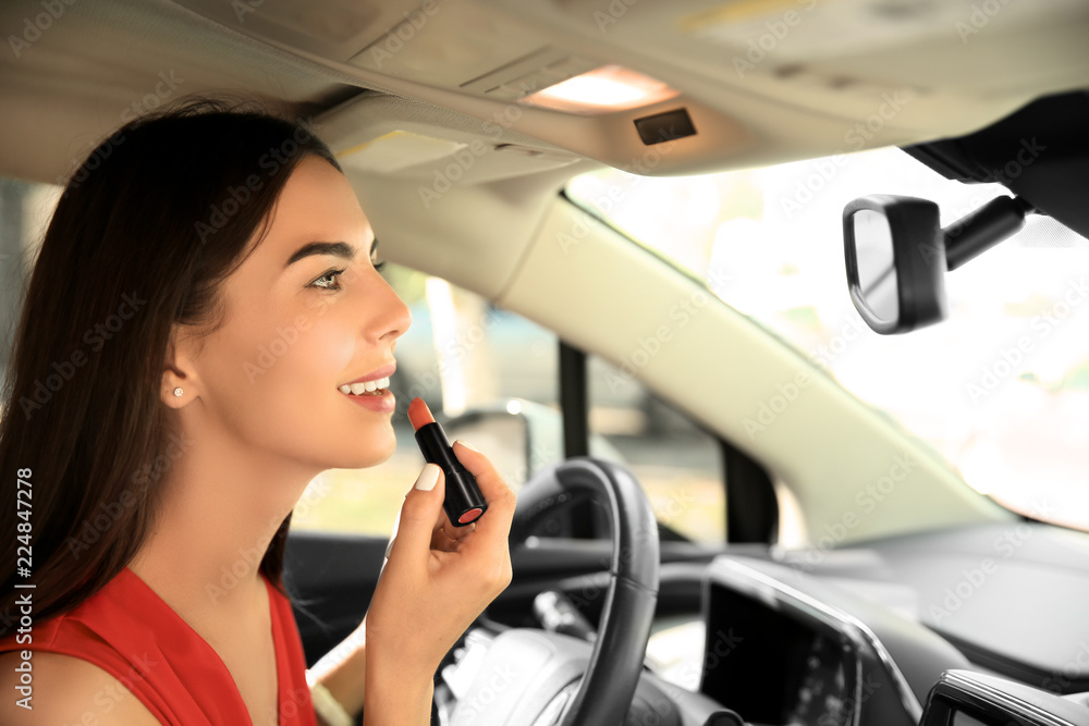 Young woman applying lipstick on drivers seat of car