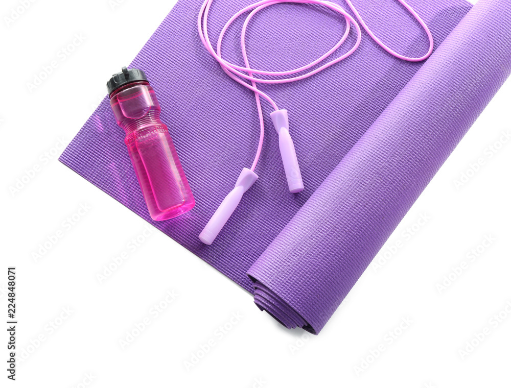 Yoga mat with jumping rope and bottle of water on white background