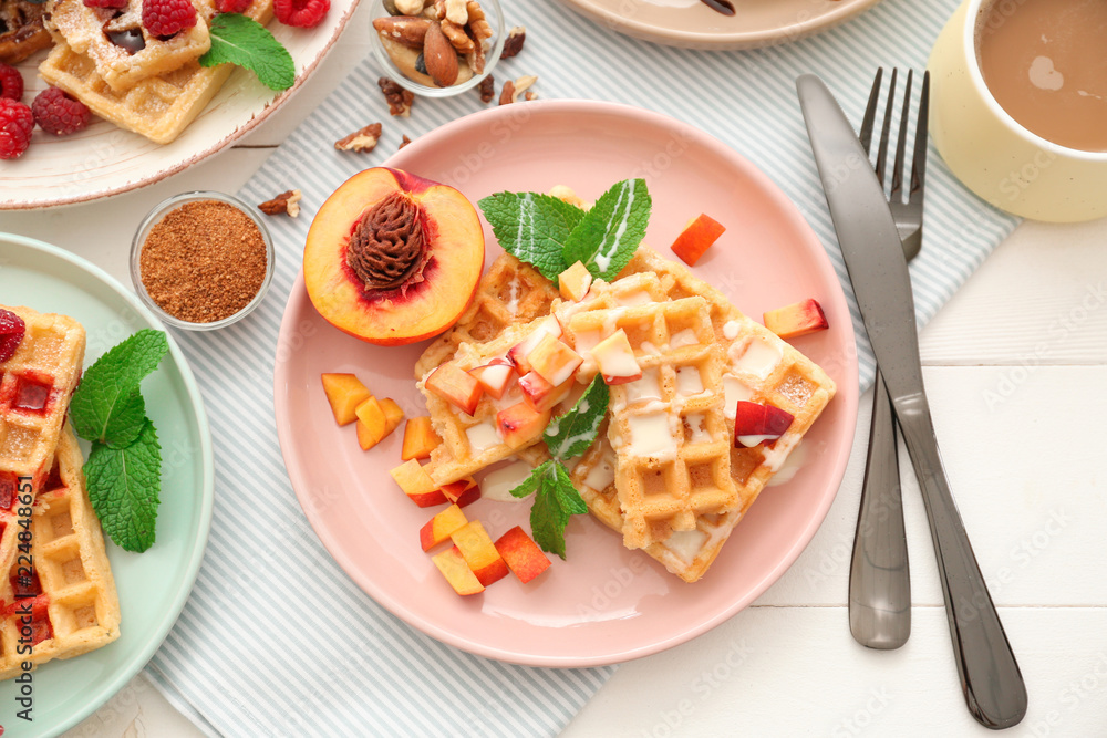 Plate with delicious waffles and peach slices on table