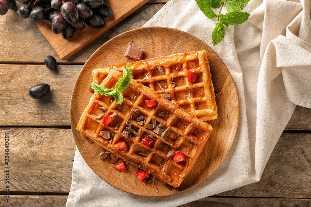 Delicious waffles with strawberries and caramel sauce on wooden plate