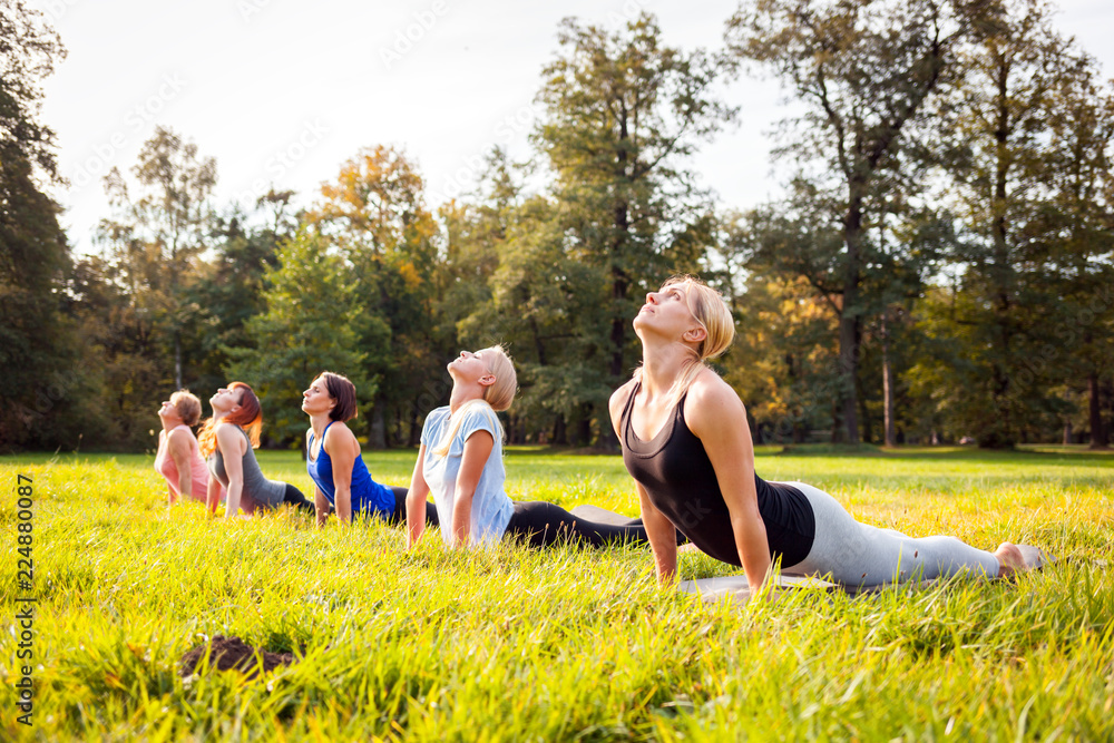 Mixed age group of people practicing yoga outside in the park