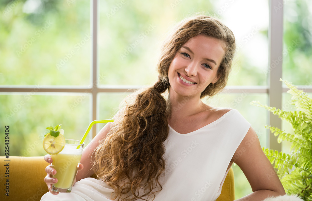 Healthy young woman lying on a couch holding a glass of fruit juice looking relaxed and comfortable