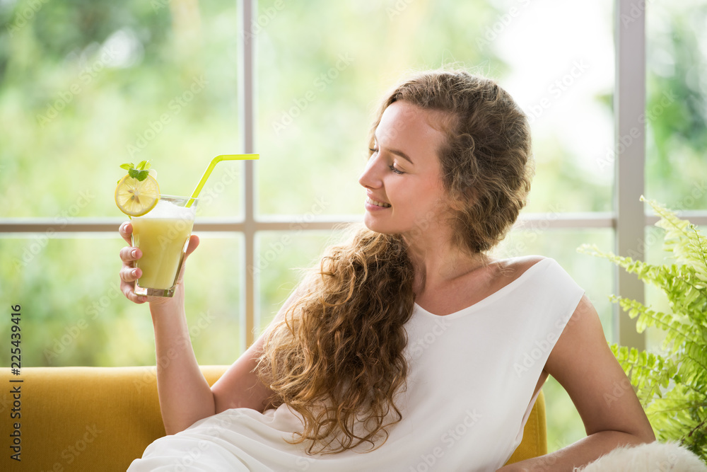 Healthy young woman lying on a couch holding a glass of fruit juice looking relaxed and comfortable