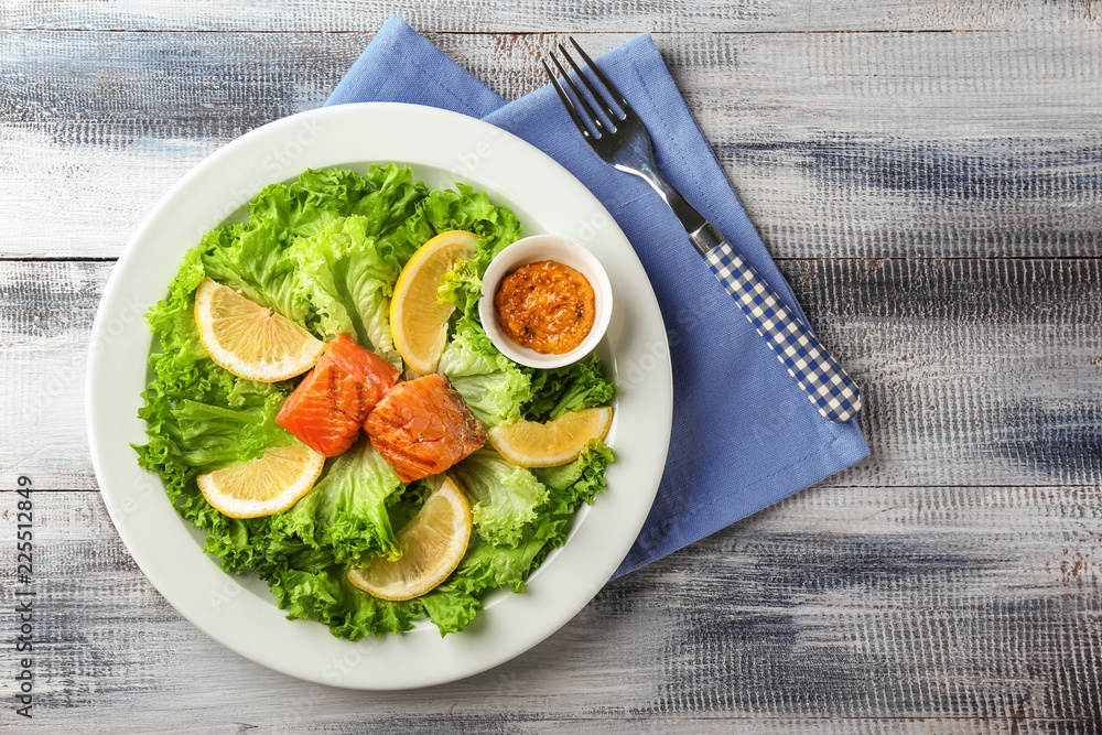 Plate with tasty salmon and fresh salad on wooden table