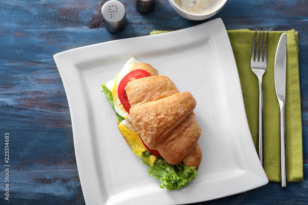 Plate with tasty croissant sandwich on color wooden table