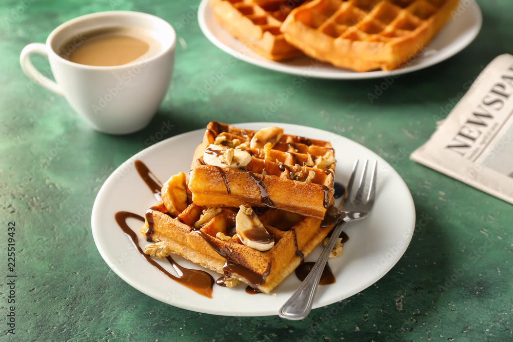 Delicious waffles with banana slices and chocolate sauce on color table