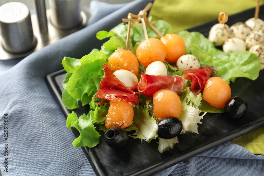 Skewers with melon, prosciutto, mozzarella and olives on plate, closeup