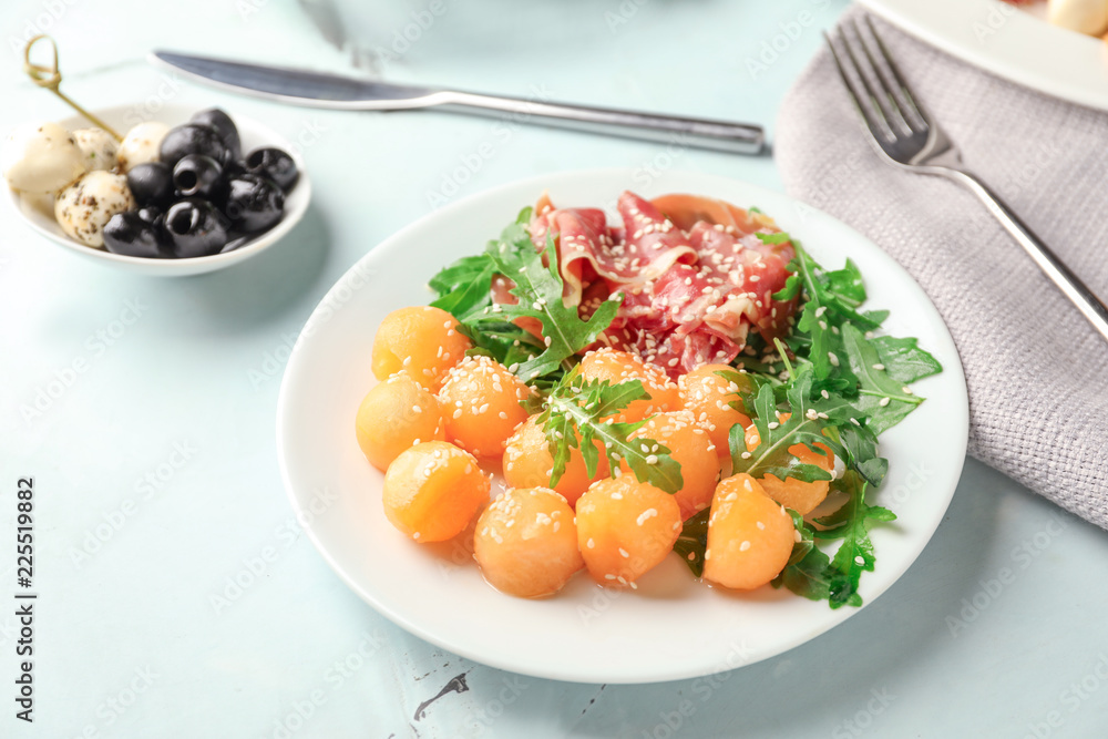 Plate with delicious melon balls and prosciutto on table