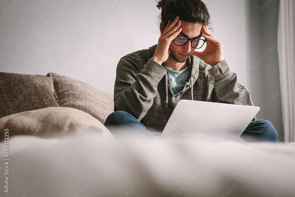 Depressed man sitting on couch with laptop